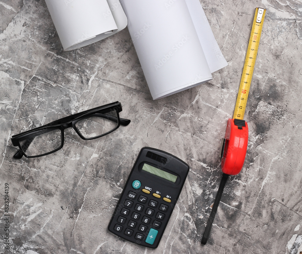 Engineer workspace. Construction helmet, rolls of drawings, calculator and glasses, ruler on gray concrete background. Top view.