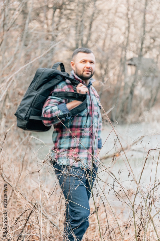 A young bearded guy with a backpack in the hat, traveller, hipster standing in the woods. A young bearded guy with a backpack in the hat, traveller, hipster standing in the woods.
