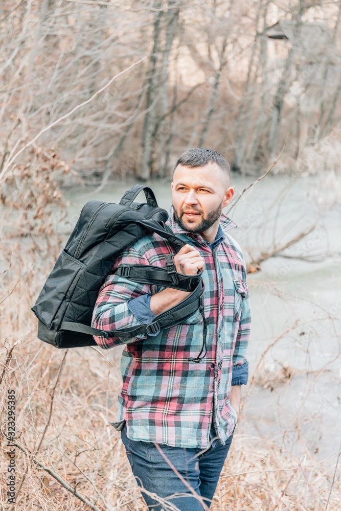 A young bearded guy with a backpack in the hat, traveller, hipster standing in the woods. A young bearded guy with a backpack in the hat, traveller, hipster standing in the woods.