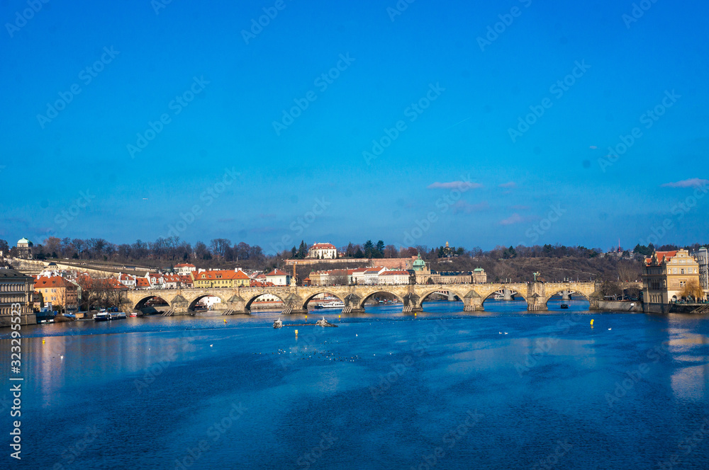 View of the Carles Bridge in Prague, Czech republic as seen from the Legion bridge overlooking Vltava river. Bright and bold blue colours of the water with birds in daylight.