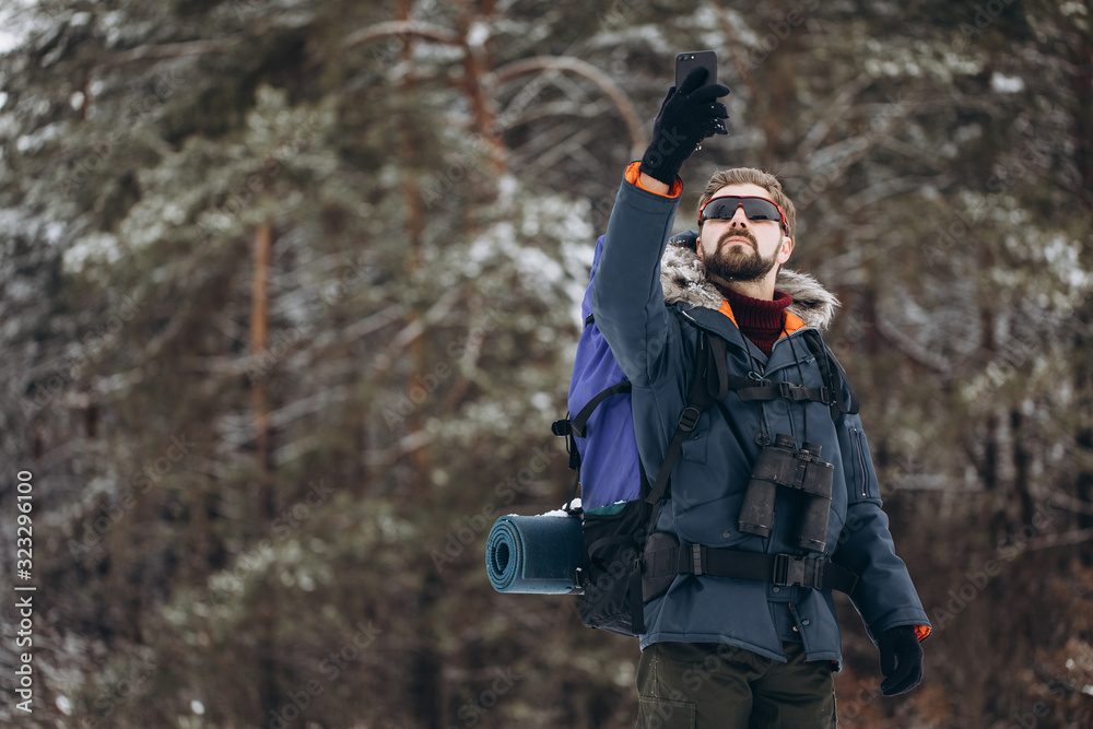 Male hiker with backpack and binoculars raising his smartphone to get connection