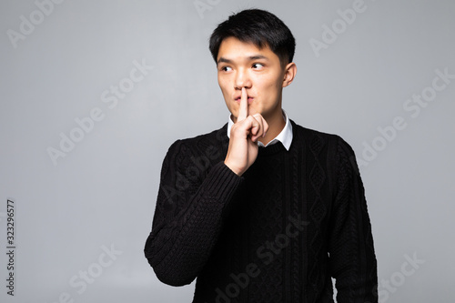 Young asian chinese man asking to be quiet with finger on lips standing over isolated white background. Silence and secret concept.