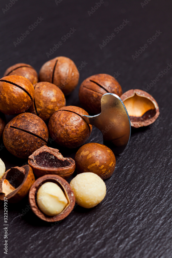 Obraz premium Whole and open macadamia nuts with key on black background.