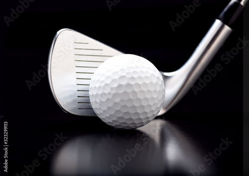 Closeup of a nine iron with a golf ball on black with reflection.