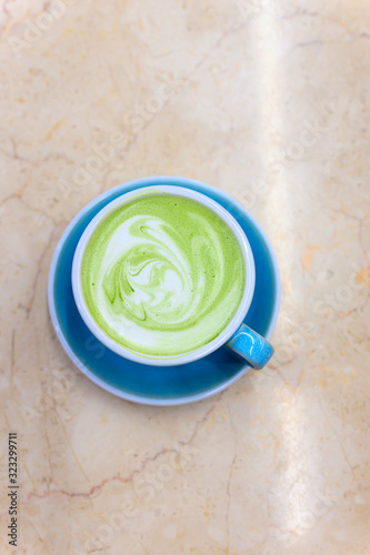 matcha green tea latte with a pattern of milk foam in a blue ceramic cup on the table. vertical photo