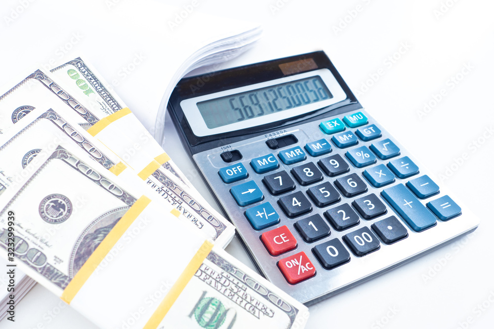 Bundles of money next to a calculator. Costing. Money to pay bills. Concept - dollars are prepared to pay taxes. Accounting audit. Counting balances in the company account. Calculate available money Bundles of money next to a calculator. Costing. Money to pay bills. Concept - dollars are prepared to pay taxes. Accounting audit. Counting balances in the company account. Calculate available money