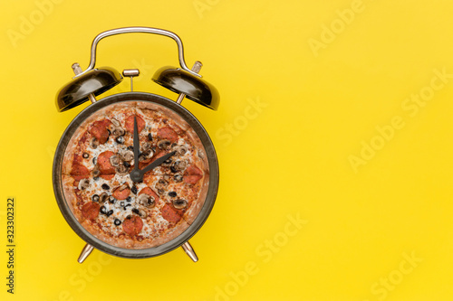 Black alarm clock with a pizza instead of a dial. Yellow background.