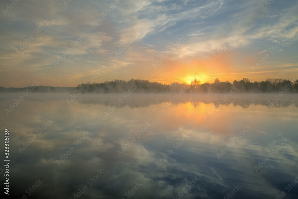 Landscape at sunrise of Whitford Lake in fog with mirrored reflections in calm water, Fort Custer State Park, Michigan, USA