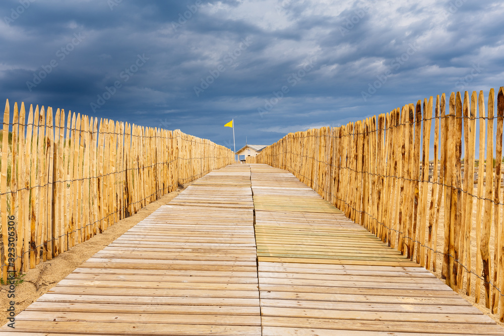 Obraz premium Heller, hölzener Strandübergang in Lacanau Océan, Frankreich, bei aufziehenden, dunklen Gewitterwolken