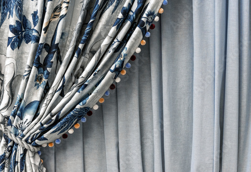 Curtain with a blue floral pattern and multi-colored pompons on the edge.