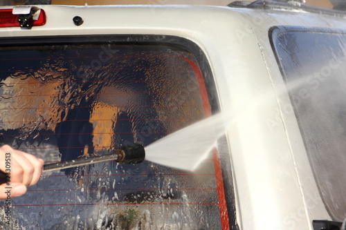 Washes thevehicle rear door glass of a silver SUV car with a high-pressure jet washer gun