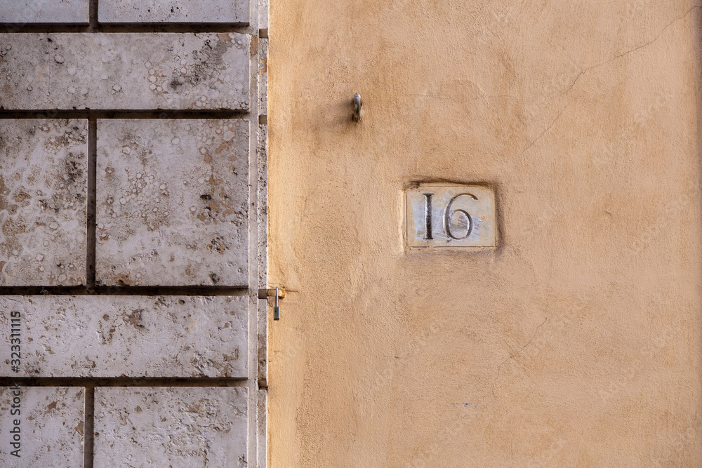 number 16, ancient house number plate on brick wall, Italy