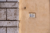 number 16, ancient house number plate on brick wall, Italy