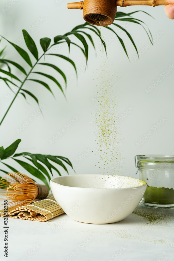 Green Tea Powder Being Poured on a Ceramic bowl. Making Japanese matcha latte tea with traditional matcha tools on white background.