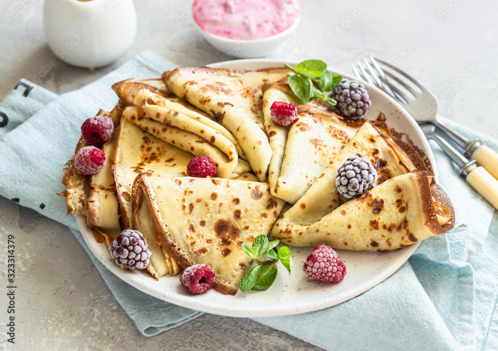 Freshly fried homemade french crepes (thin pancakes) on a ceramic plate with frozen raspberries, blackberries and mint for breakfast or dessert.