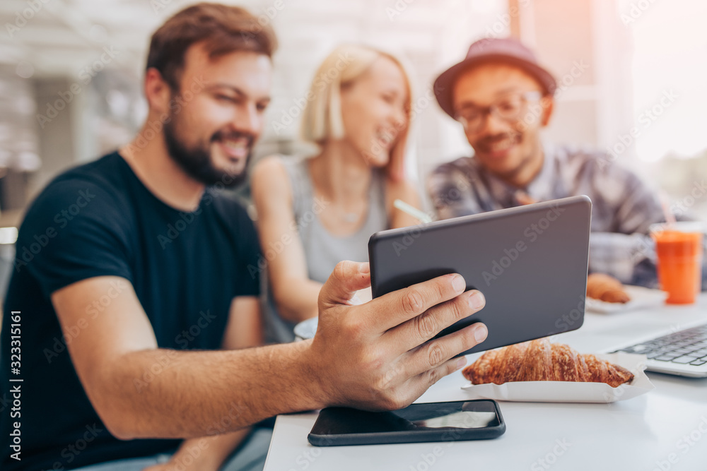 Man sitting with friends and using tablet in cafe Man sitting with friends and using tablet in cafe