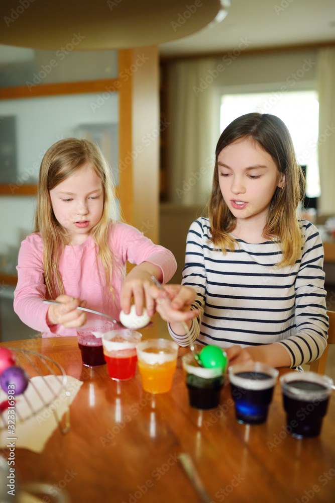 Two cute young sisters dyeing Easter eggs at home. Children painting colorful eggs for Easter hunt. Kids getting ready for Easter celebration. Two cute young sisters dyeing Easter eggs at home. Children painting colorful eggs for Easter hunt. Kids getting ready for Easter celebration.