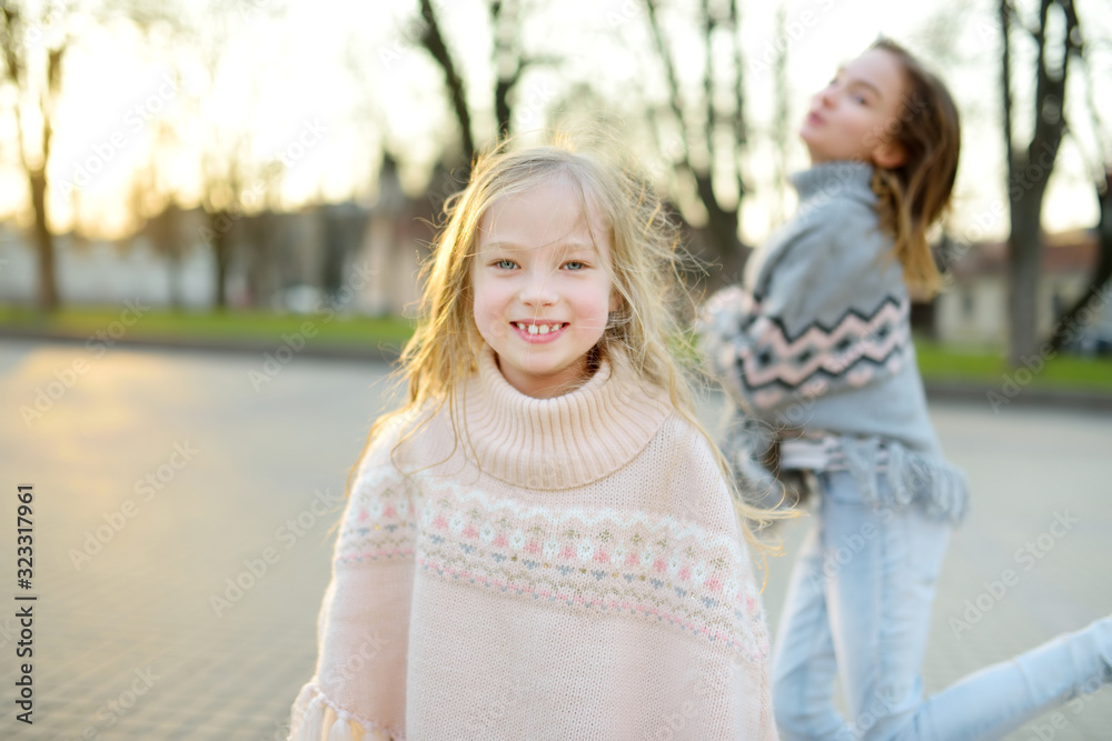 Two cute young sisters having fun together on beautiful spring day in a city. Active family leisure with kids.