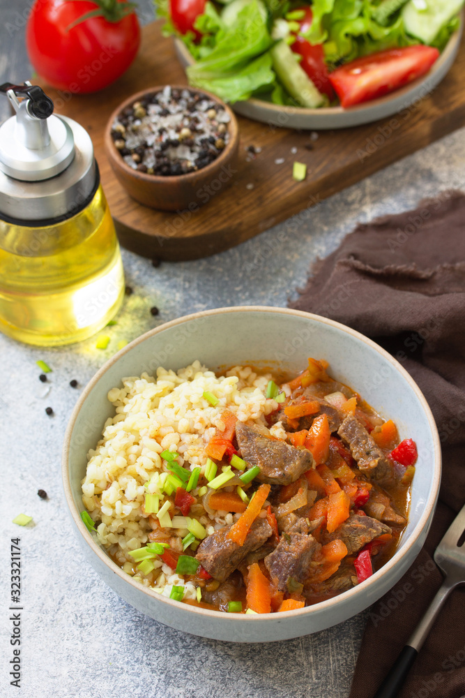 Healthy eating concept. Beef stewed with vegetables in bulgur sauce and fresh vegetable salad on a light stone table top. Healthy eating concept. Beef stewed with vegetables in bulgur sauce and fresh vegetable salad on a light stone table top.