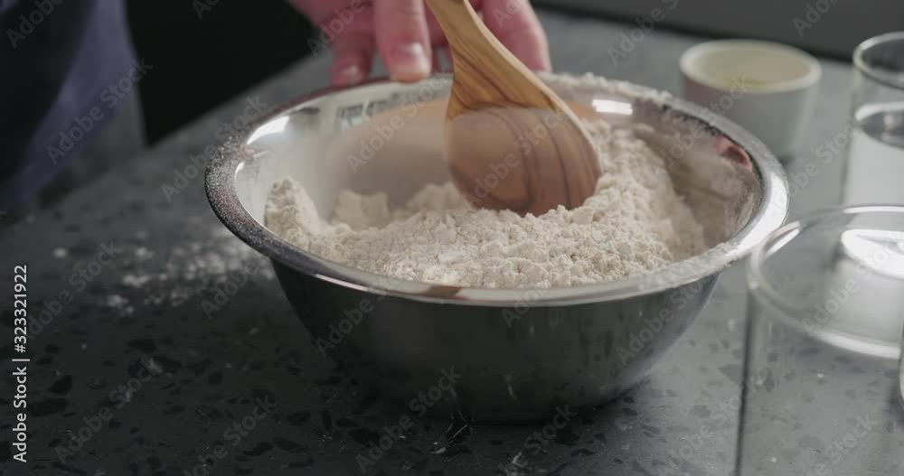 Slow motion man mixing dry ingredients with flour in steel bowl on concrete countertop Slow motion man mixing dry ingredients with flour in steel bowl on concrete countertop