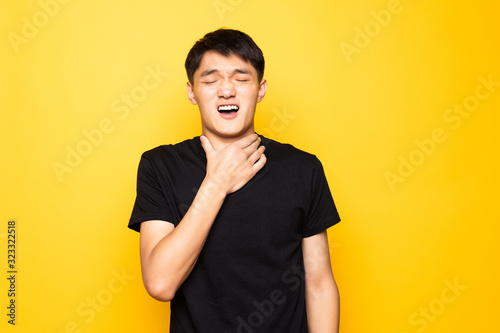 Young asian chinese man shouting and suffocate because painful strangle standing over isolated yellow background . Health problem. Asphyxiate and suicide concept.