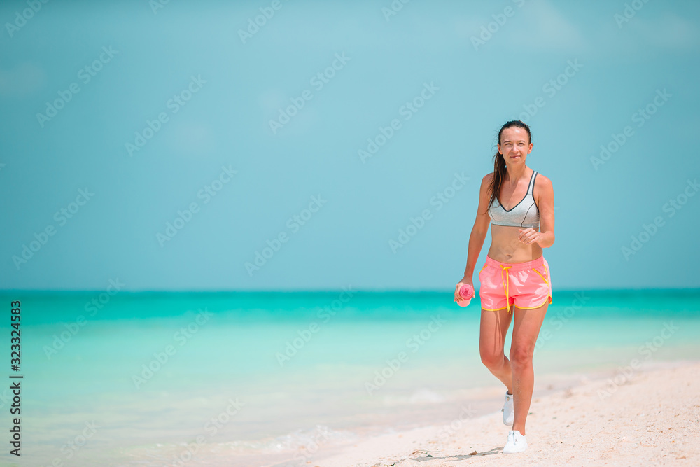 Fit young woman doing exercises on tropical white beach in her sportswear Fit young woman doing exercises on tropical white beach in her sportswear