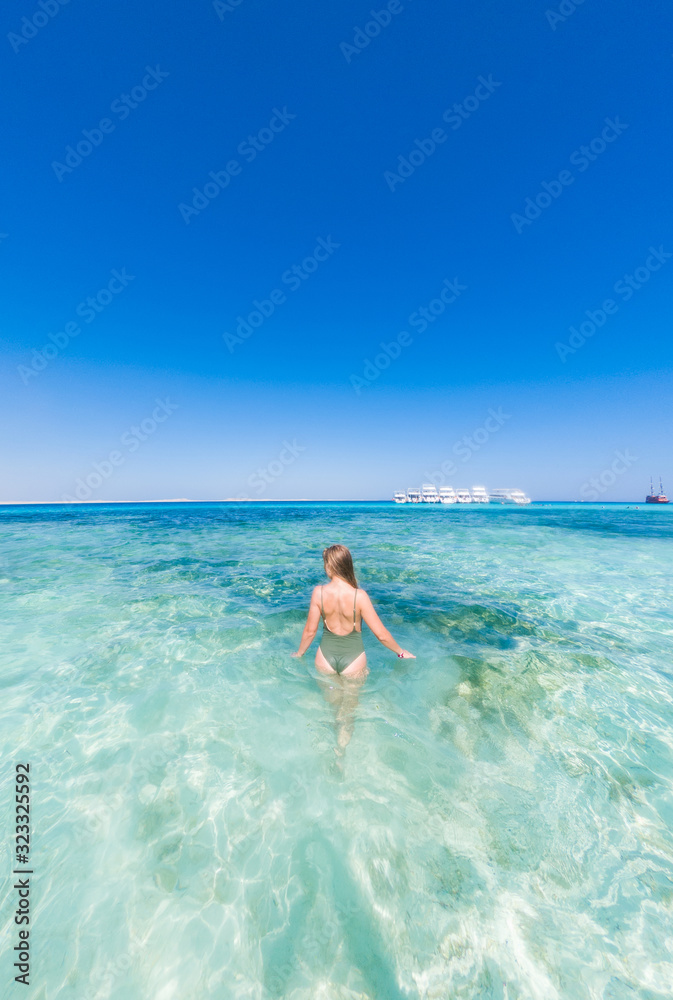 A girl in a green swimsuit to bathe in the blue water of the red sea. It's sunny outside