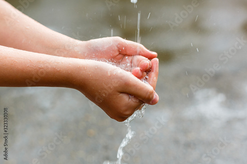 Water pouring in children's hands on nature background, environment issues © Flower_Garden