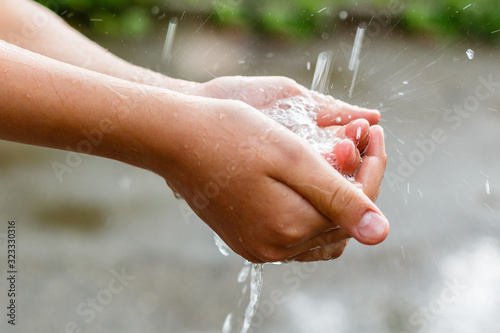 Water pouring in children's hands on nature background, environment issues © Flower_Garden