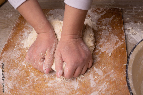 A woman kneads the dough. Plywood cutting board, wooden flour sieve and wooden rolling pin - tools for making dough.
