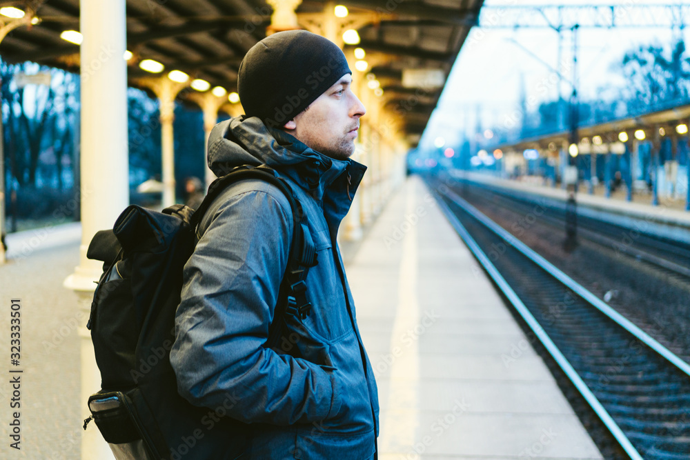Sopot Fast Urban Railway station. young man standing and waiting train on platform. tourist travels by train. Portrait Of Caucasian Male In Railway Train Station. traveler with backpack waiting train Sopot Fast Urban Railway station. young man standing and waiting train on platform. tourist travels by train. Portrait Of Caucasian Male In Railway Train Station. traveler with backpack waiting train