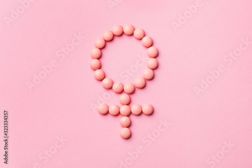 pink medicine tablets shaped as gender symbol on pastel rose background, venus sign, top view, flat lay