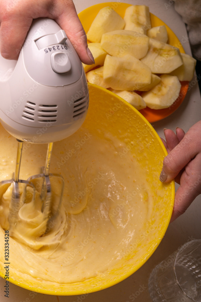 Fototapeta A woman mixes the ingredients for a pie in a yellow bowl with an electric mixer.
