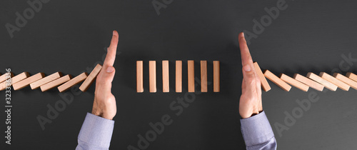 businessman protects his investment with two hands from falling dominoes photo