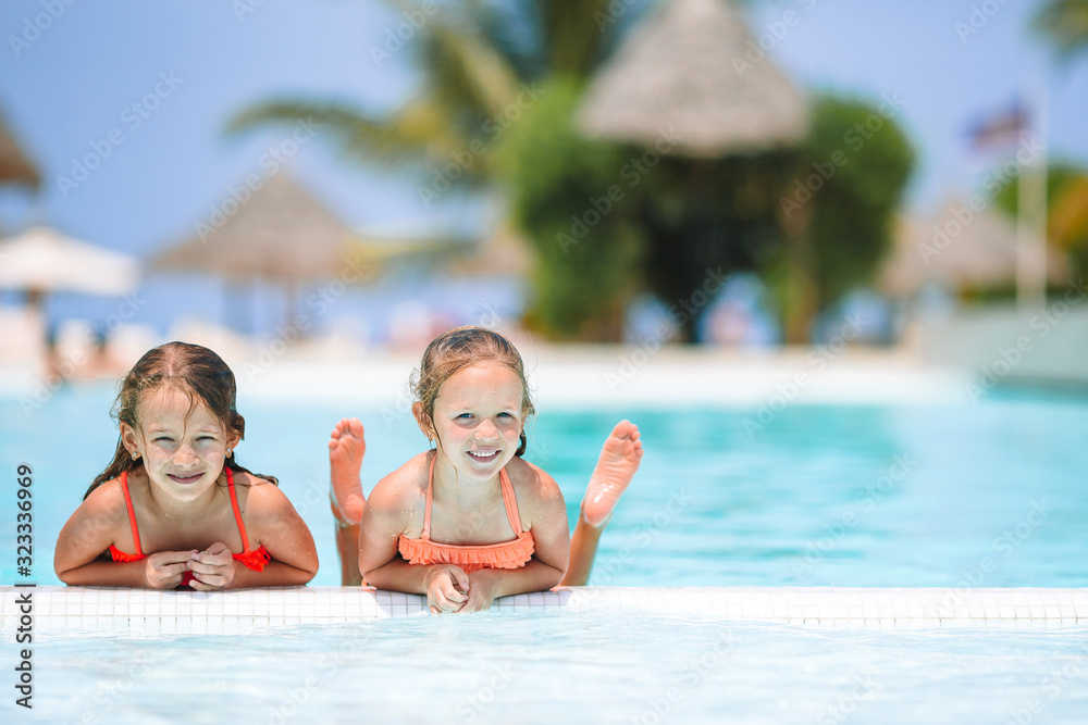 Adorable little girls playing in outdoor swimming pool on vacation Adorable little girls playing in outdoor swimming pool on vacation