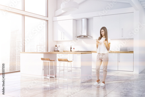 Woman with phone in white kitchen with bar