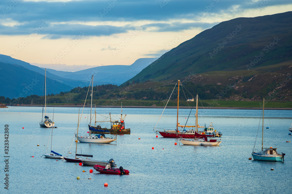 Φωτογραφία Boats that are anchored in Loch Broom off the harbor of Ullapool, Scotland, glow in the light from a sunset