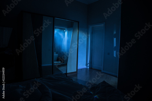 A creepy bedroom scenery, Silhouette of scary person standing reflected in mirror with mist and toned light.