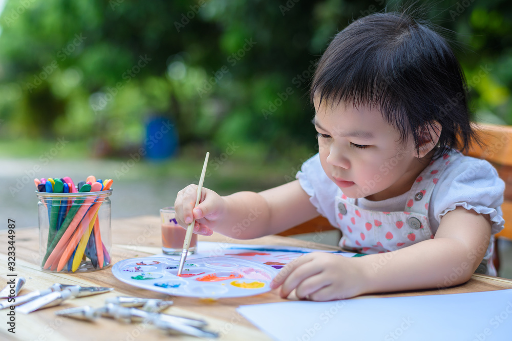 Cute little Asian girl in a white dress is drawing with painting fun Cute little Asian girl in a white dress is drawing with painting fun
