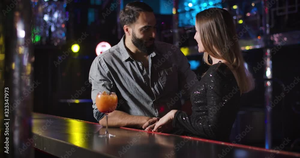 Confident young Middle Eastern man coming to charming Caucasian girl dancing next to bar counter. Handsome guy flirting with beautiful woman in night club. Cinema 4k ProRes HQ.