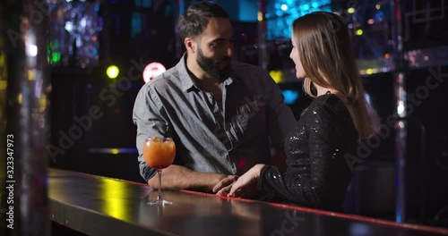 Confident young Middle Eastern man coming to charming Caucasian girl dancing next to bar counter. Handsome guy flirting with beautiful woman in night club. Cinema 4k ProRes HQ. photo
