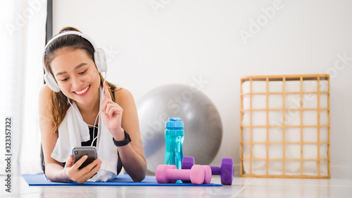 Asian woman listening to music with headphone and smartphone after play yoga and exercise at home background with copy space.Exercise for Lose weight  increase flexibility And tighten the shape.