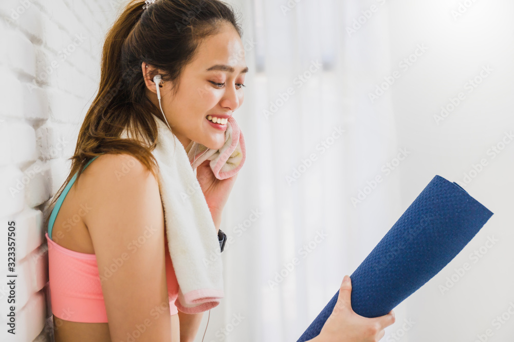 Asian beautiful woman resting and holding yoga mat after play yoga and exercise on white brick wall background with copy space.Exercise for Lose weight, increase flexibility and tighten the shape. Asian beautiful woman resting and holding yoga mat after play yoga and exercise on white brick wall background with copy space.Exercise for Lose weight, increase flexibility and tighten the shape.
