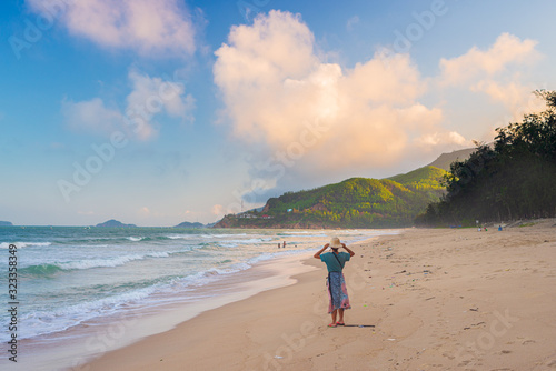 Woman with traditional vietnamese hat looking at view on tropical beach. Quy Hoa Quy Nhon Vietnam travel destination, central coast between Da Nang and Nha Trang. sunset dramatic sky