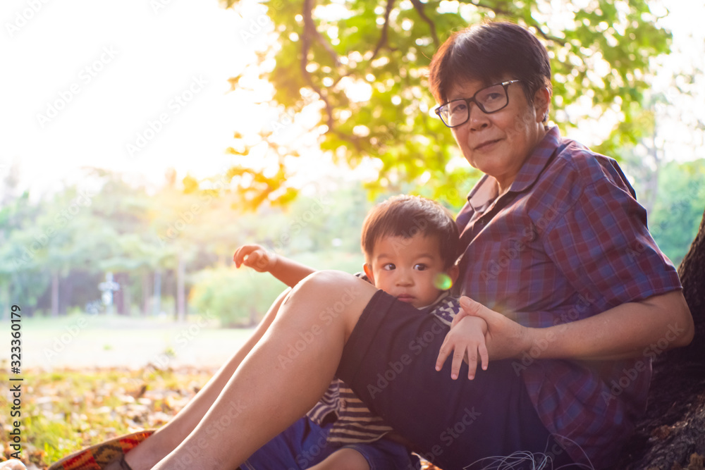Senior elderly Grandmother Playing with grandson baby boy under tree in city park sunset light Senior elderly Grandmother Playing with grandson baby boy under tree in city park sunset light