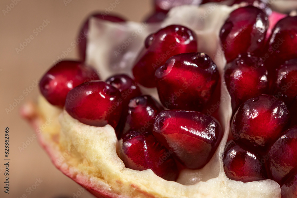 Close-up: A slice of peeled pomegranate lies on a light wood kitchen board. Bright red grains of pomegranate shine beautifully. Studio photography under artificial lighting with two light sources. Close-up: A slice of peeled pomegranate lies on a light wood kitchen board. Bright red grains of pomegranate shine beautifully. Studio photography under artificial lighting with two light sources.