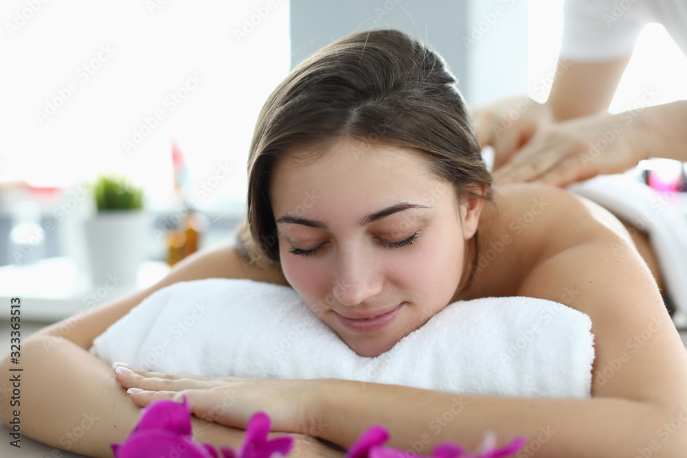 Massage in salon using relaxation techniques. Beautiful woman lies table for cosmetic procedures, on roller made towels, masseur makes relaxing massage to client. Massage room interior. Massage in salon using relaxation techniques. Beautiful woman lies table for cosmetic procedures, on roller made towels, masseur makes relaxing massage to client. Massage room interior.
