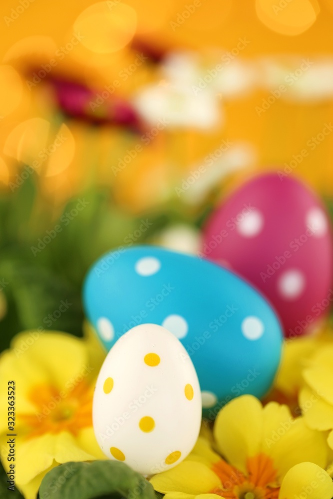 Easter holiday.Easter eggs and spring flowers. Decorative eggs set on yellow primrose flowers on bright orange with bokeh background.Spring festive background.