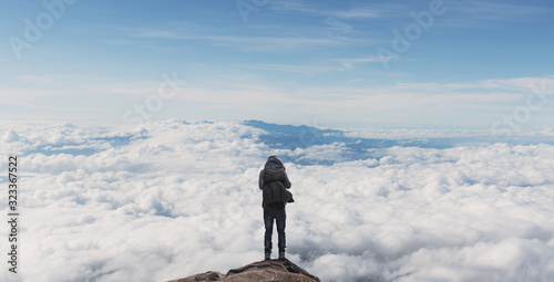 a man with backpack standing on mountain top over clouds. Success, achievement and outdoor adventure concepts