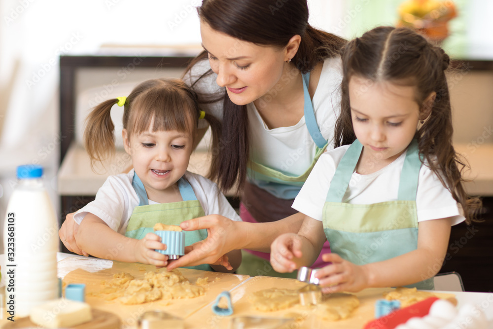 Mother and kids daughters weared aprons making cookies together Mother and kids daughters weared aprons making cookies together